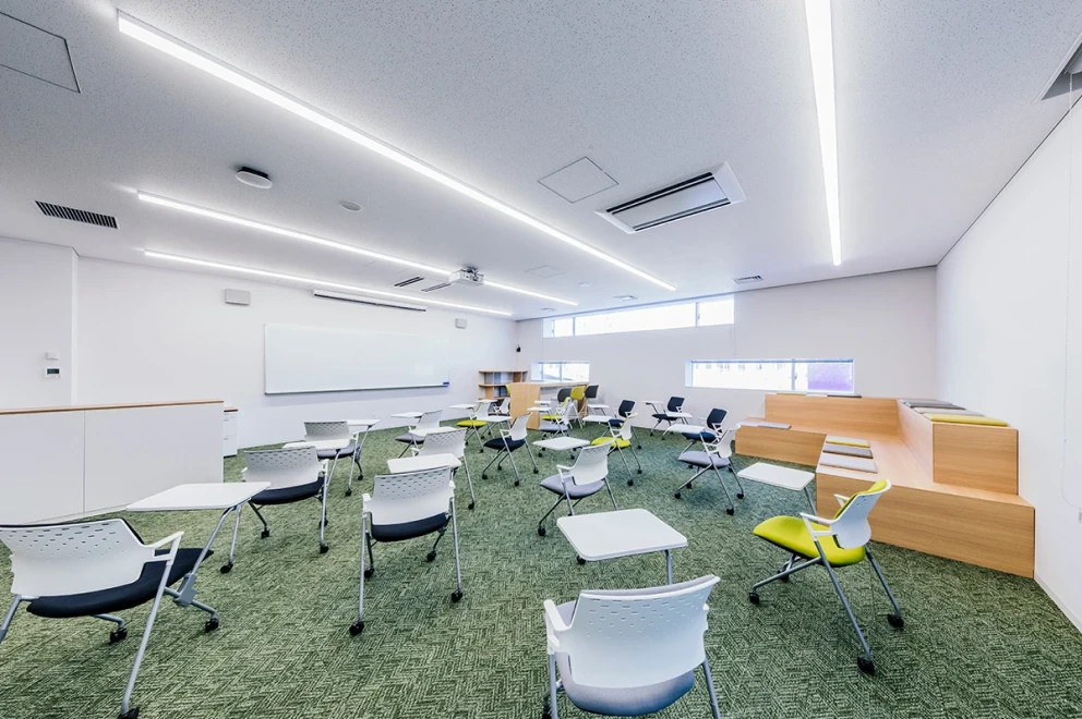 グローバル教室の写真。ホワイトボードの向けて円形に椅子が配置されている。壁際には2段のベンチも配置されている。